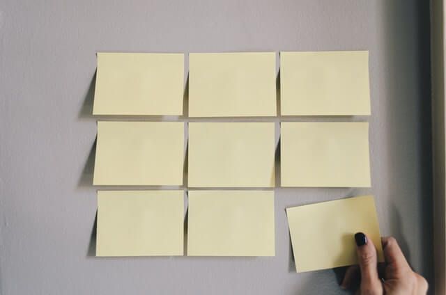 Nine blank post-its attached to a wall, with a hand placing the ninth. 